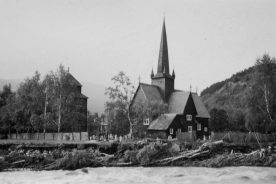 Historisk sort hvitt bilde av flommen i 1938, elven i forgrunnen som grever seg inn mot kirkebakken.