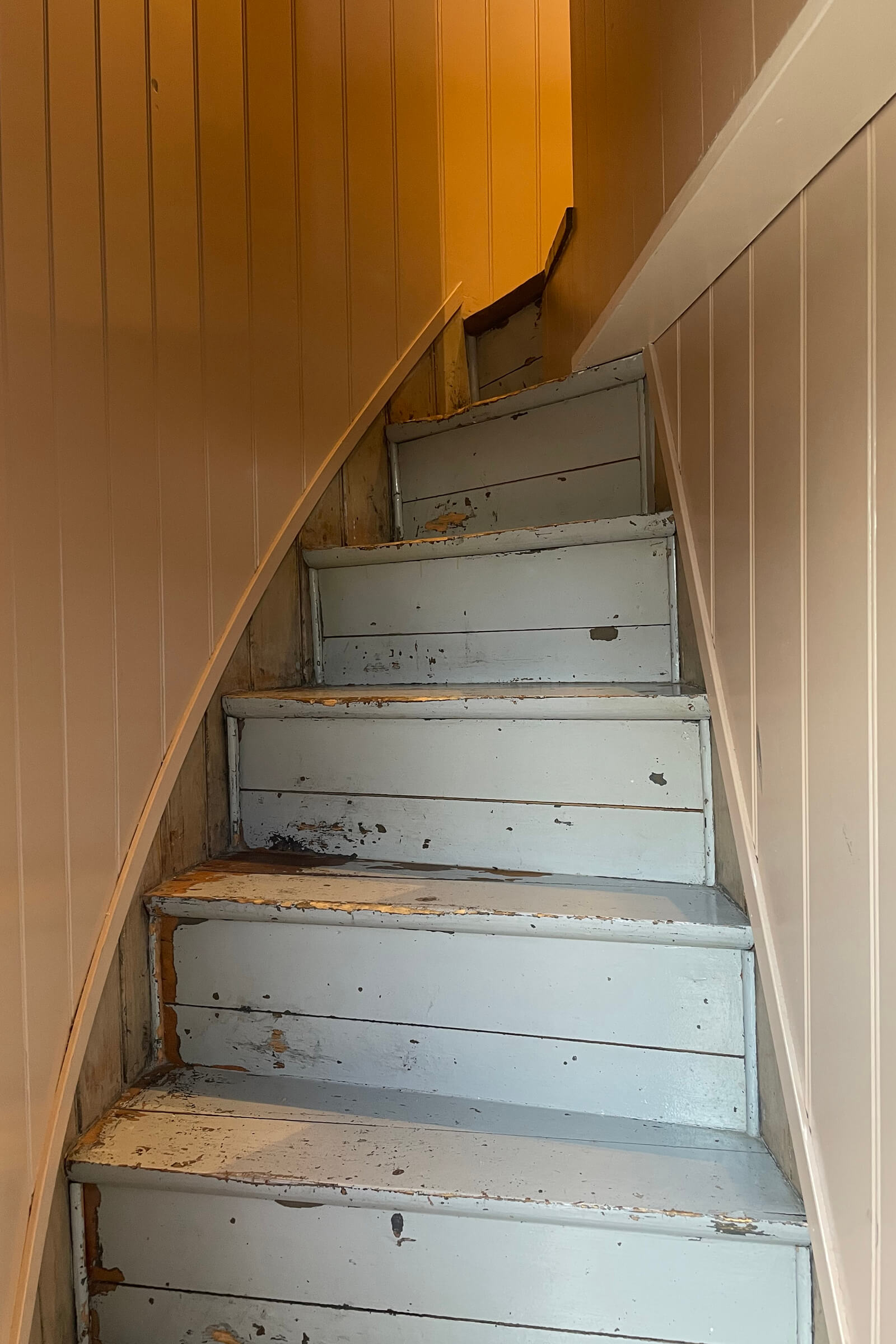 Trappen opp til soverommet er malt i lyseblå, veggene har en varm gul perlestaffpanel. Trappen smalner av mot toppen.